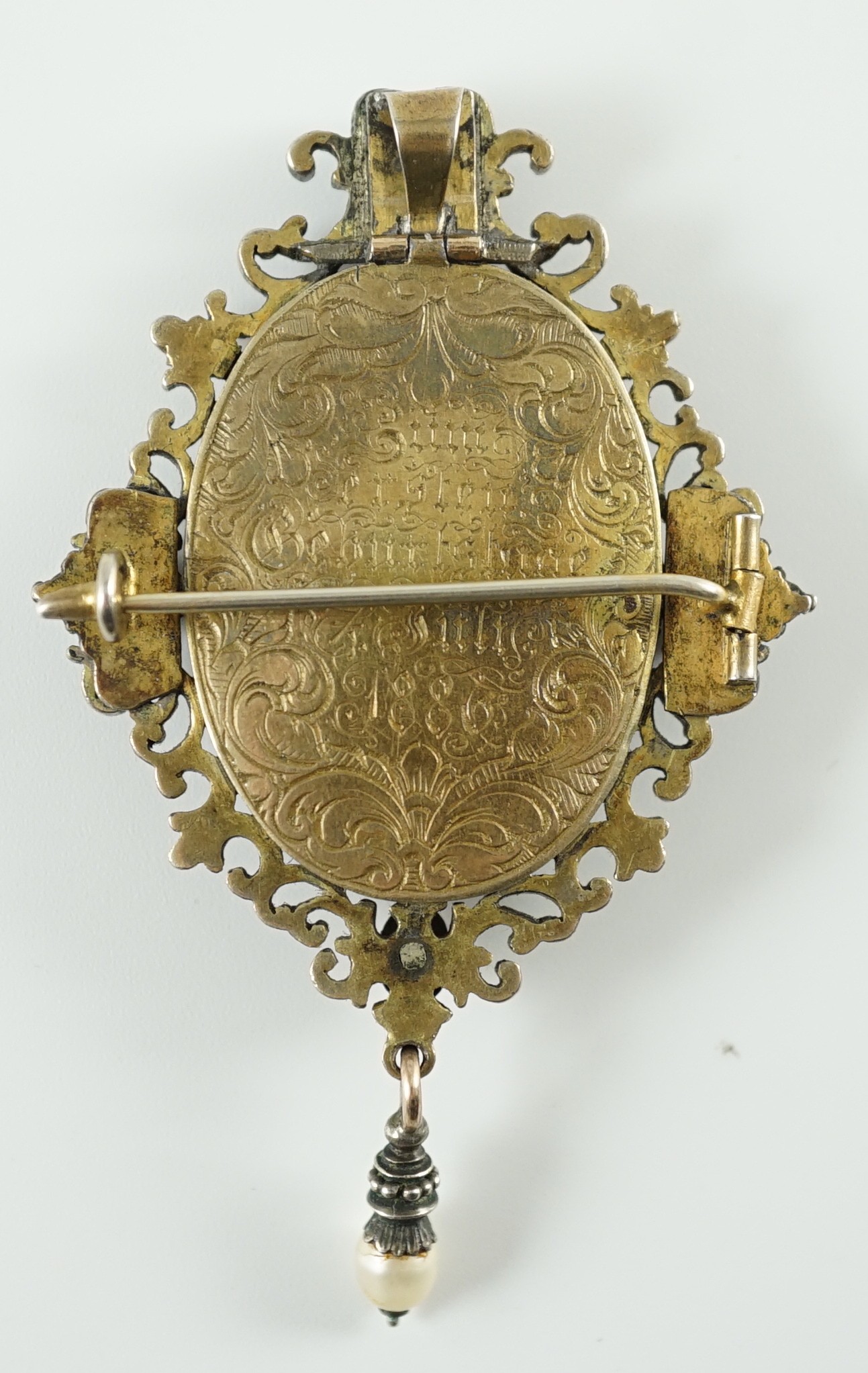 A Victorian oval gold, silver and cloisonné enamelled locket pendant, worked with a heron beneath wisteria, within a border mounted with pearls and foil backed garnets, the reverse inscribed and dated 1886